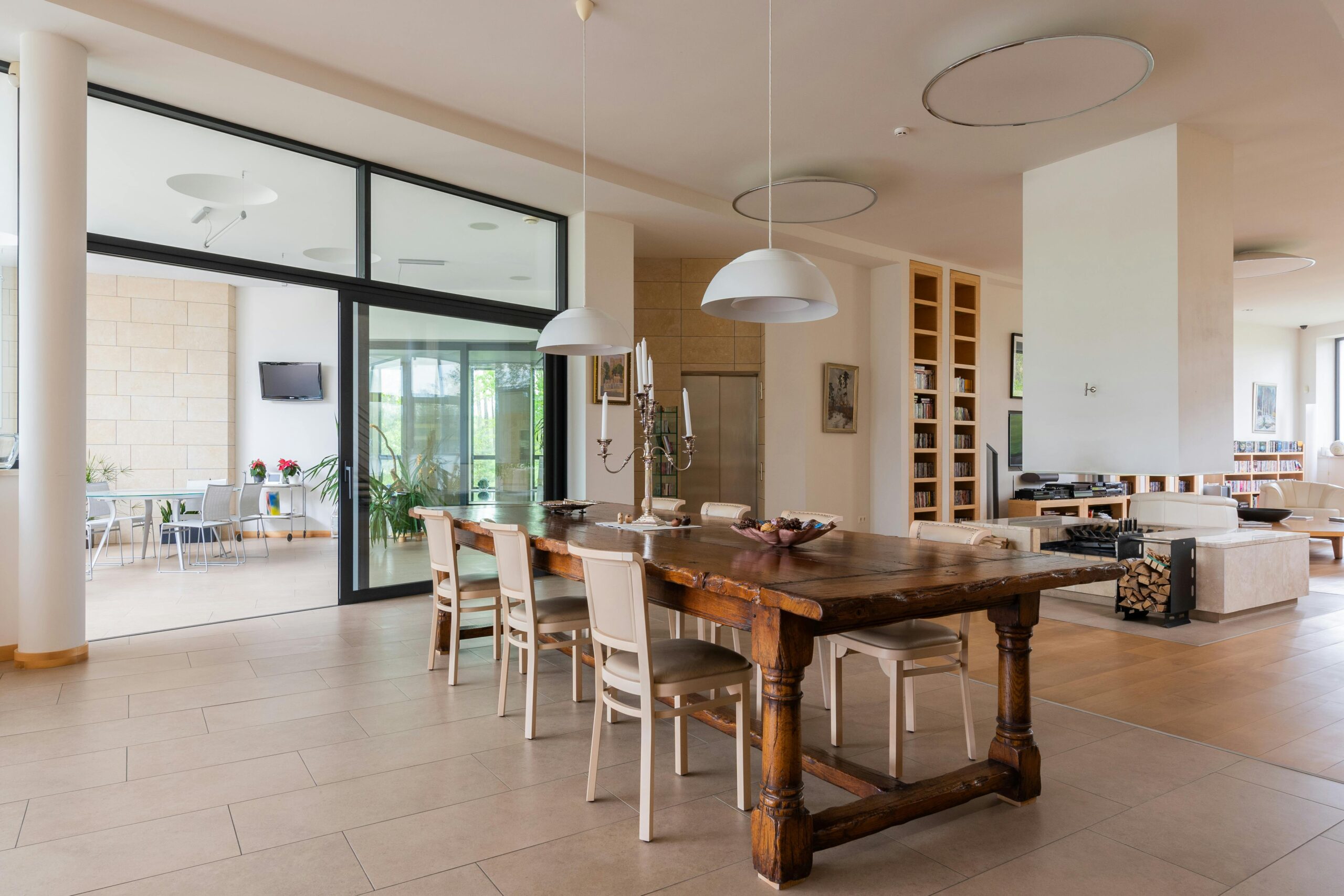 Wooden table with candlestick and chairs placed near modern living room in stylish apartment with hanging lamps against doorway overlooking terrace