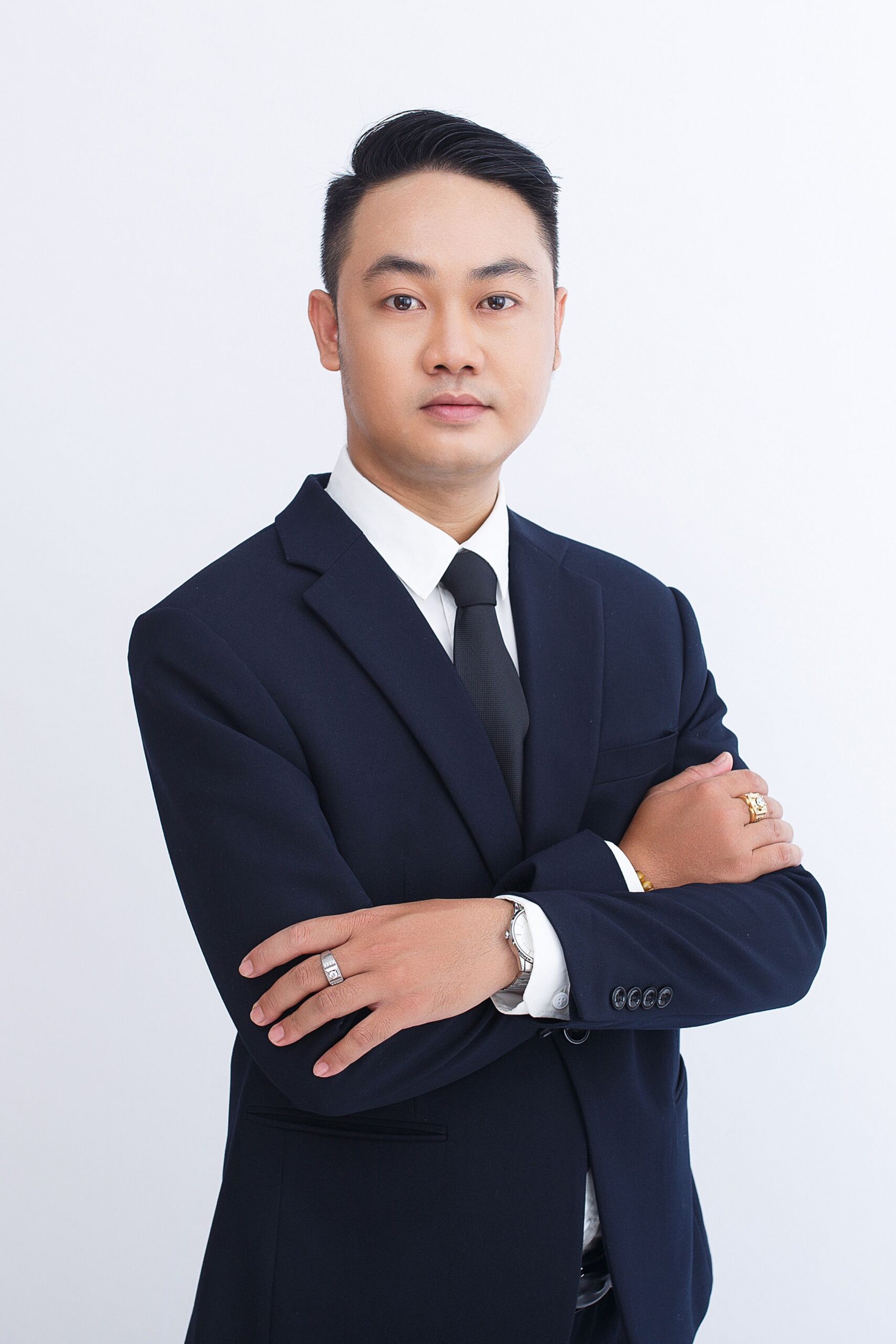 A confident businessman standing in a suit with crossed arms against a plain background.